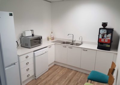 small office kitchenette with espresso machine featuring white doors and countertops