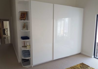 bespoke designs built in cupboards in gloss white with slide doors and corner shelving design