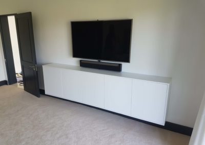 custom suspended TV entertainment unit in bedroom for widescreen TV with gloss white finish and no door handles