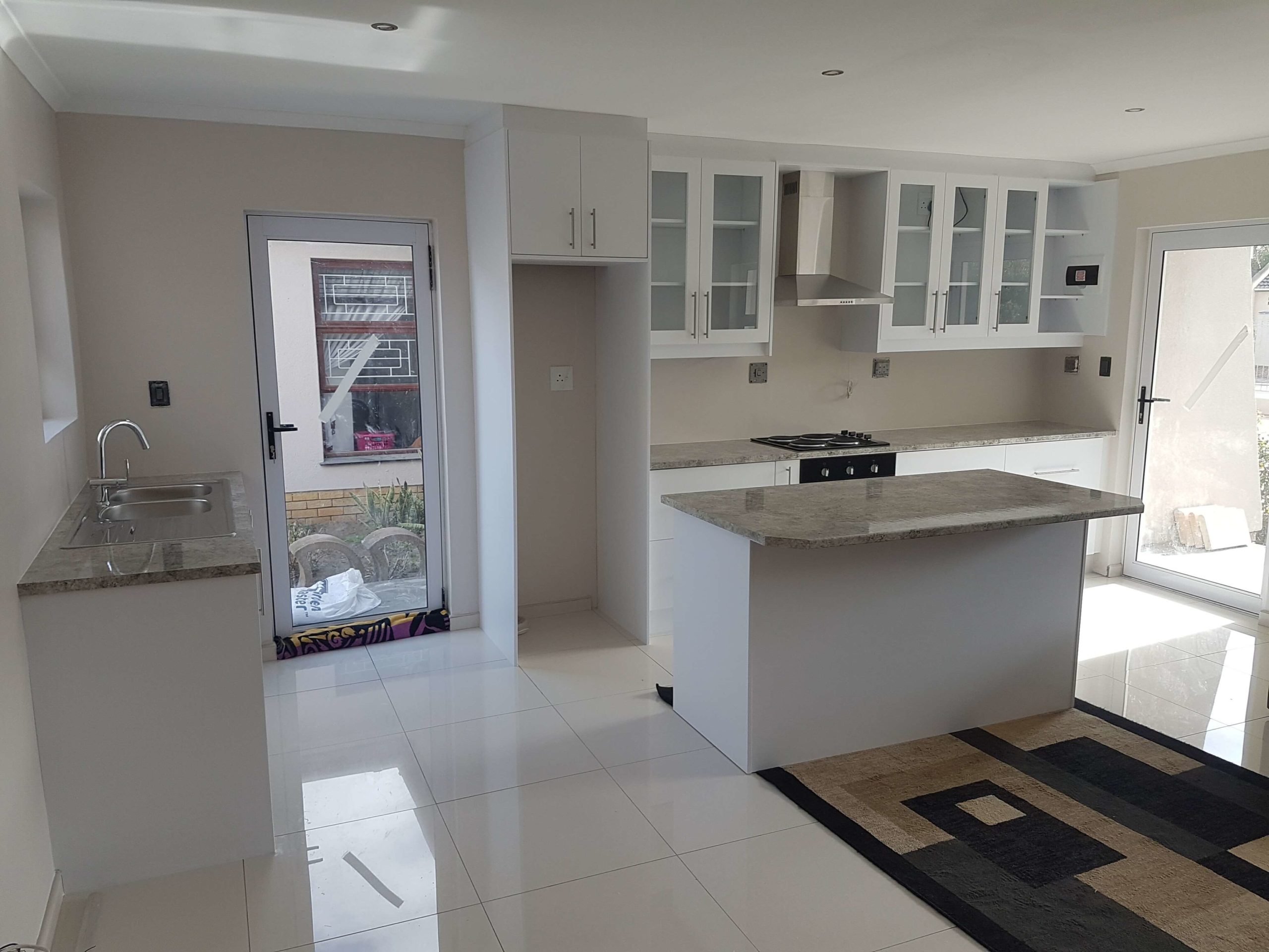 white kitchen cupboards with grey counters and clear glass doors and an island in the centre 2