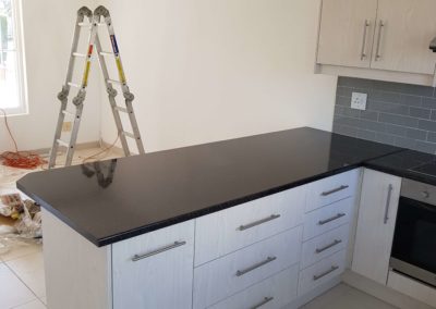 custom kitchen built out with dark grey counters and light grey cupboards and a wood grain textured finish and grey tiles 5